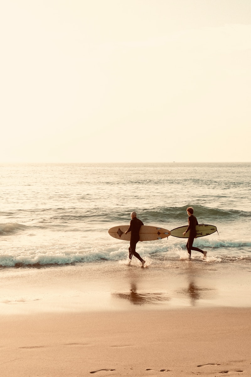 Two surfers head into the ocean with their boards.