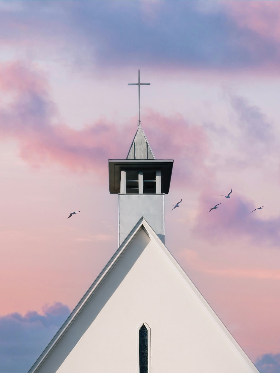 White church steeple against a pastel sky with birds.